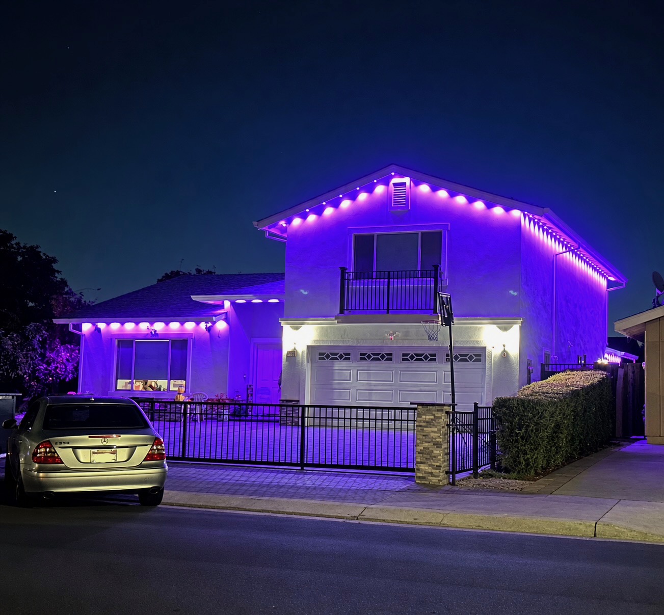 Two-story home at dusk with vibrant purple permanent LED eave lighting across the facade and balcony