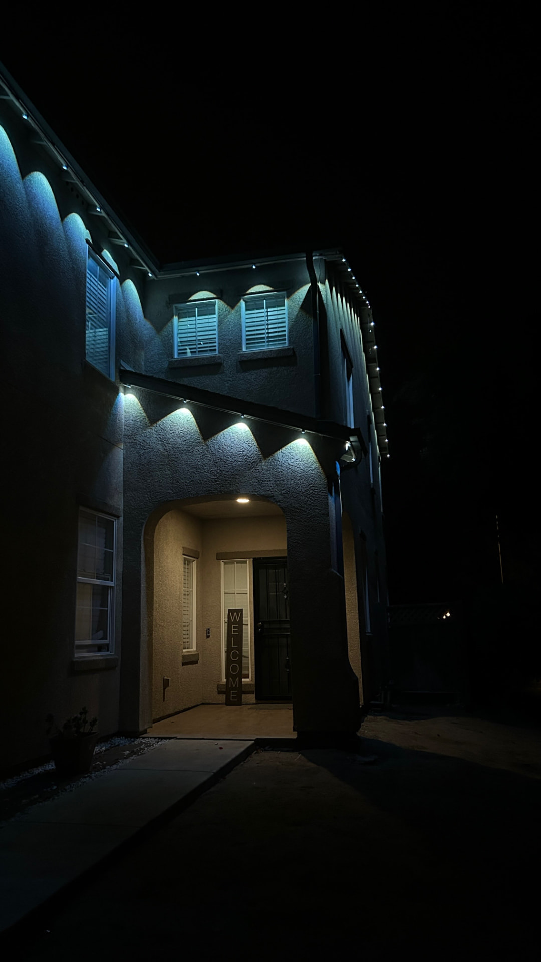Home entrance at night with cool white permanent LED soffit lighting and a welcome sign