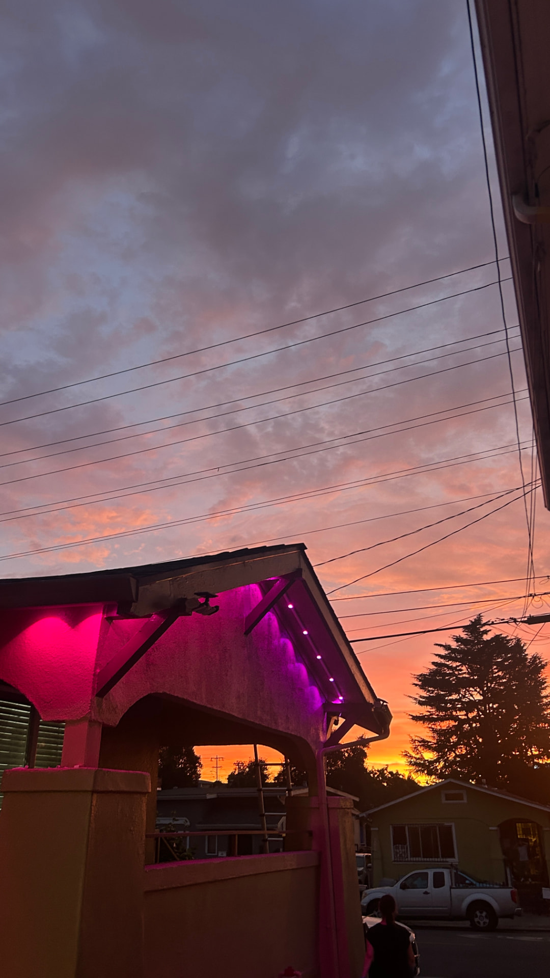 Home eave glowing with pink and purple permanent LED lighting under a colorful sunset sky