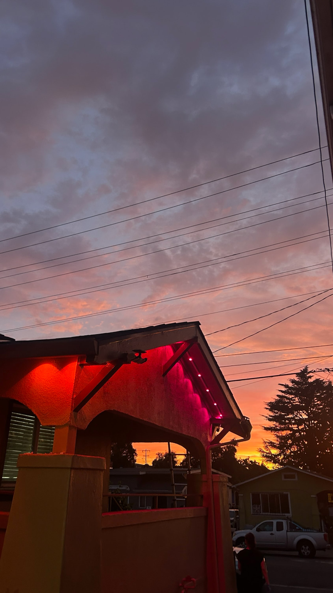 Home gable lit with vivid red and pink permanent LED lighting against a sunset sky