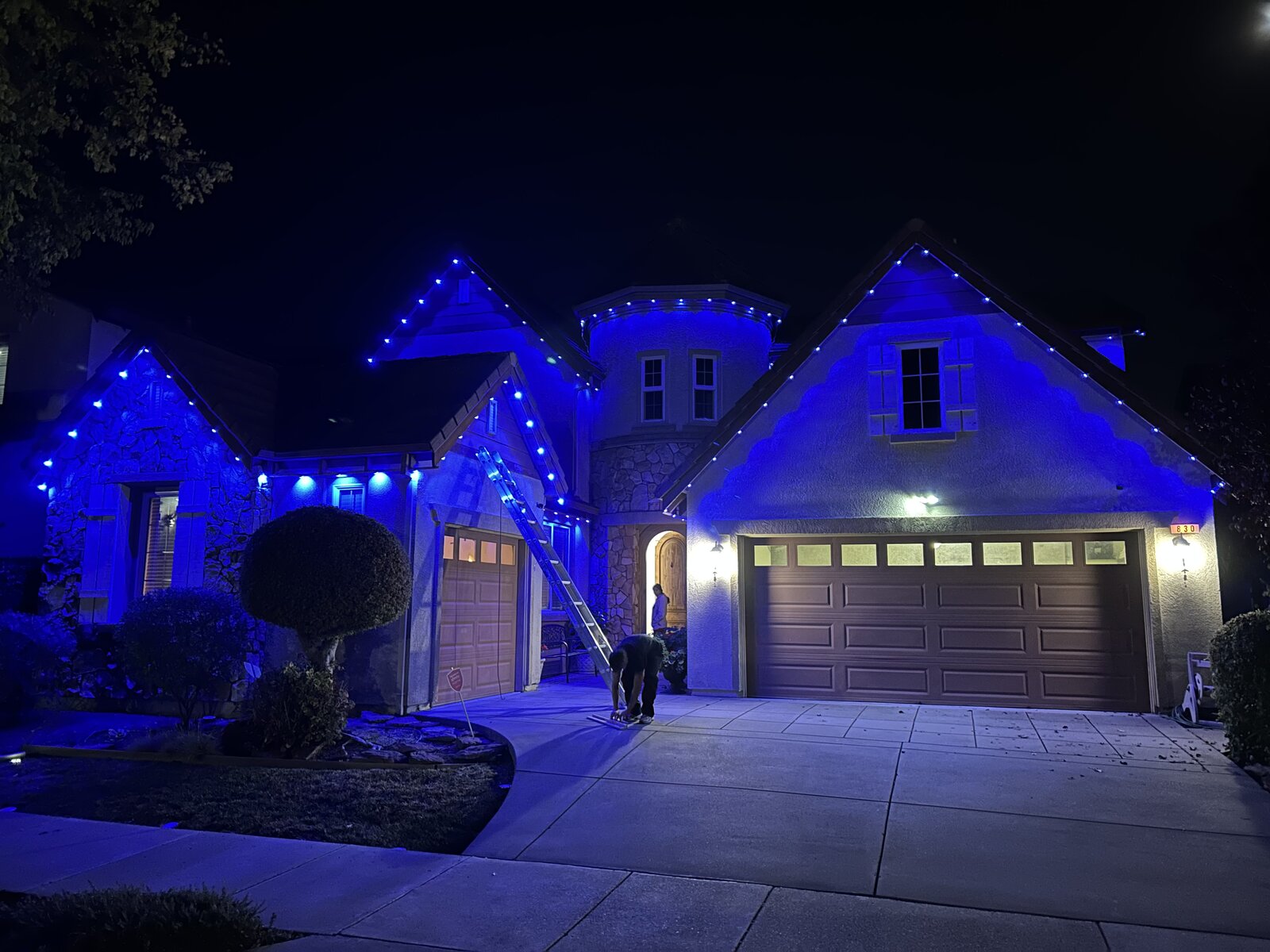 Two-story home at night with vivid blue permanent LED lighting across the gables and turret