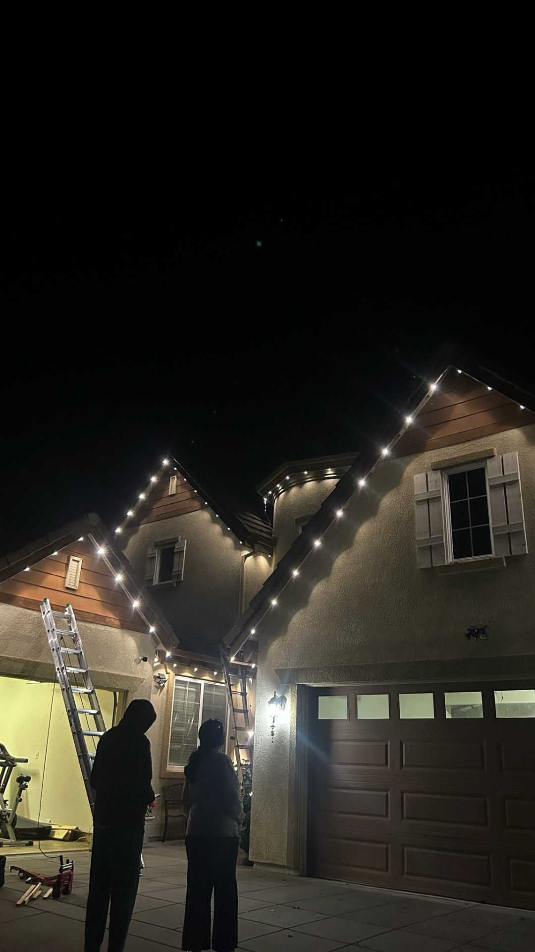Permanent LED lighting install with warm white roofline lights and a ladder at the gable