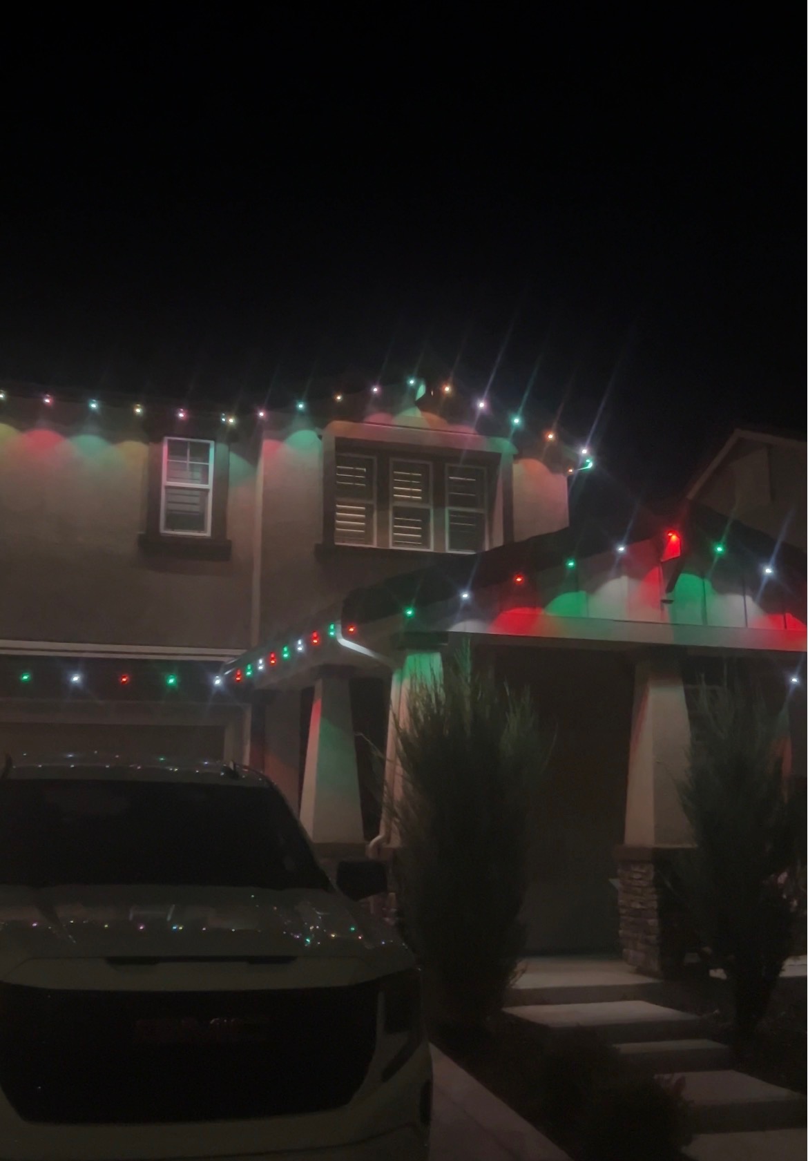 Two-story stucco home at night with red, green and white permanent LED roofline lighting above the garage and porch