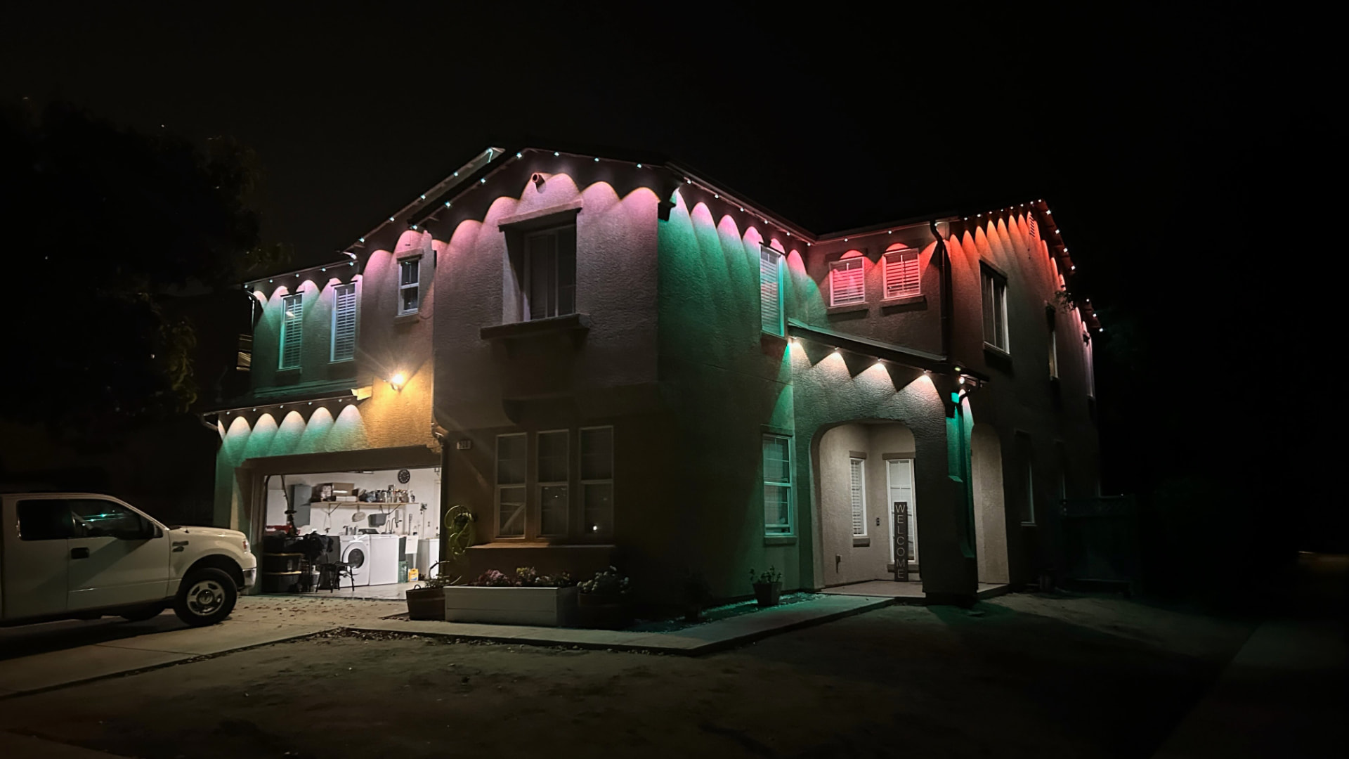 Two-story home at night with multicolor permanent LED lighting beams across the facade